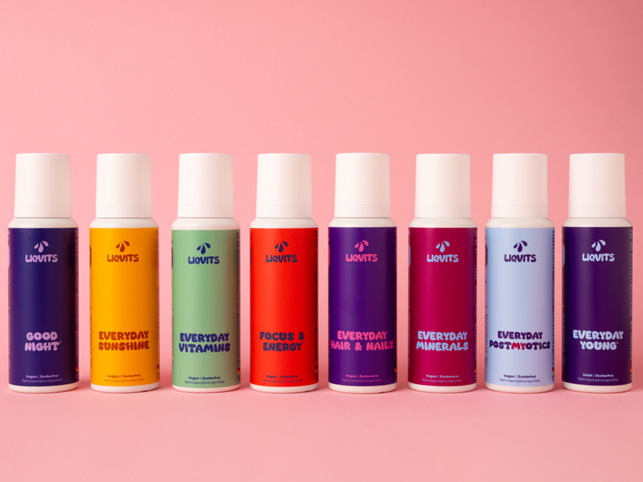 Auf dem Bild sind viele Fläschchen auf rosafarbenen Hintergrund in unterschiedlichen bunten Farben. Der Deckel aller Fläschchen immer weiß.