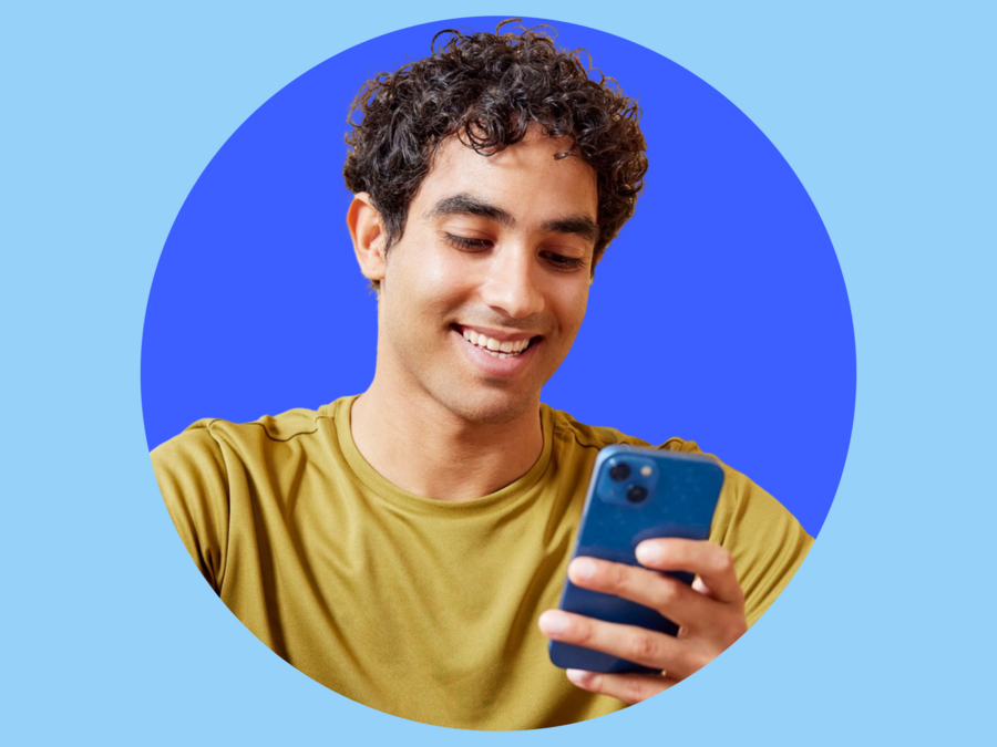 Mann mit braunen locken und einem lächeln hält ein Handy in der linken Hand und trägt ein gelbes Shirt