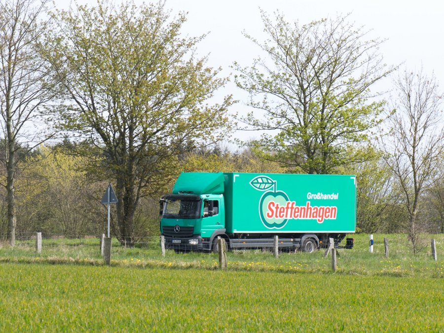 Ein grüner LKW von Steffenhagen fährt gerade über eine Landstraße. Drum herum sind Bäume und Wiesen.