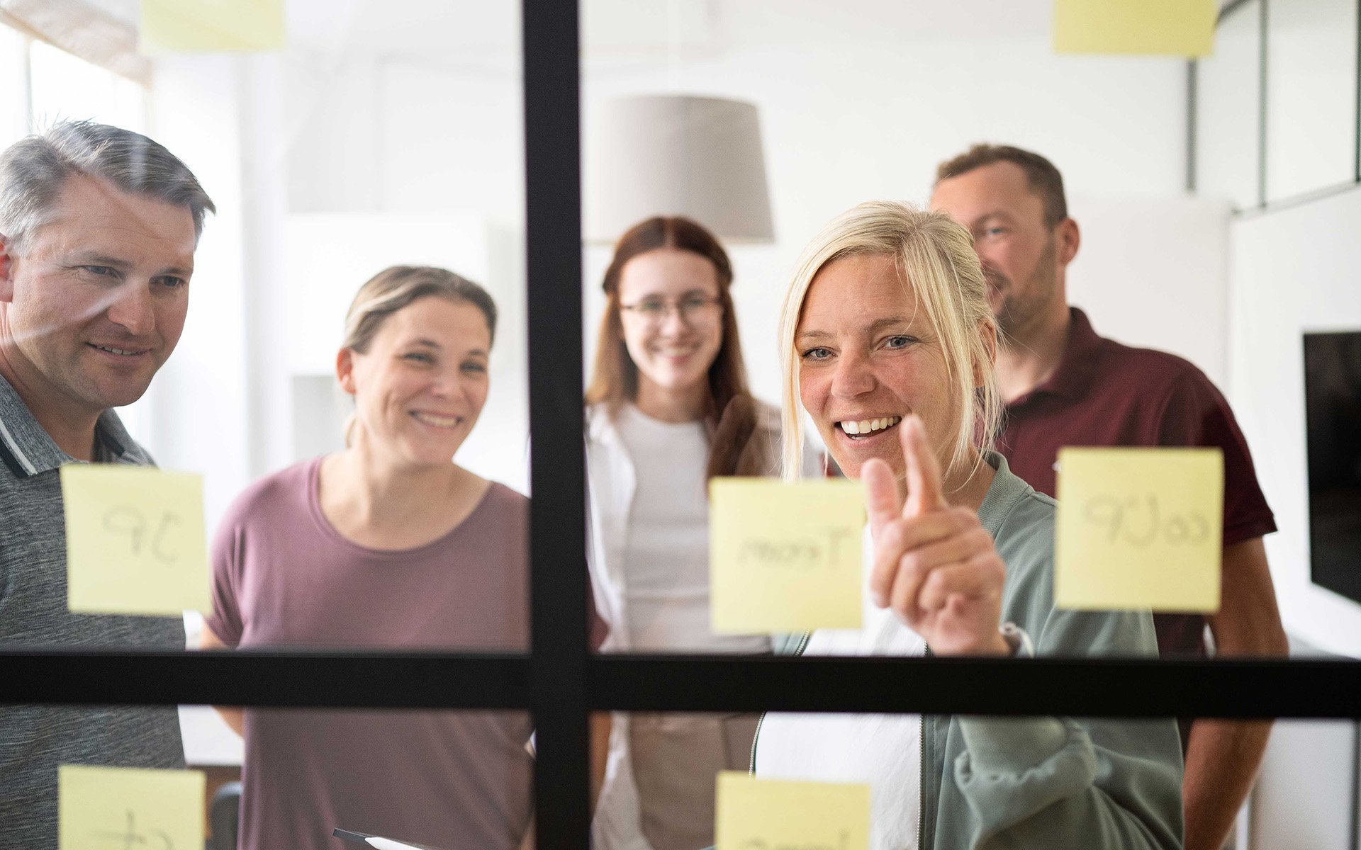 Fünf Menschen stehen vor einer Glaswand, an der Post Its kleben.