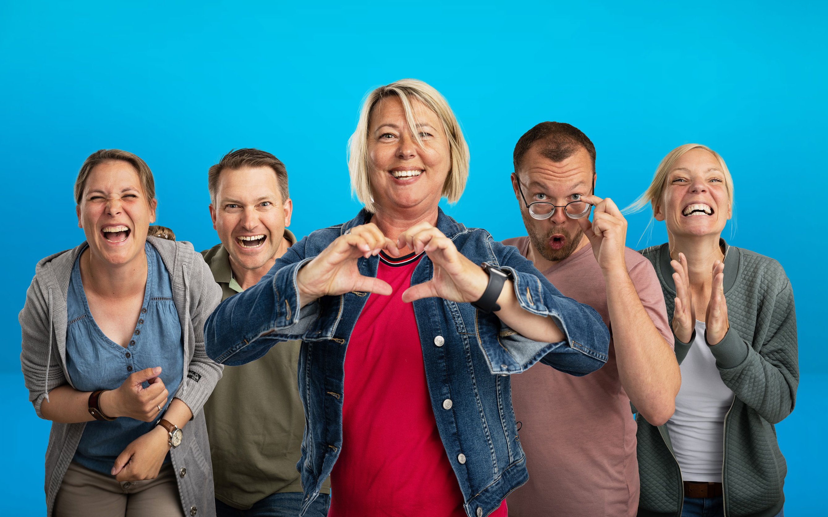 fünf Personen gestikulieren und lachen ausgelassen vor blauem Hintergrund 