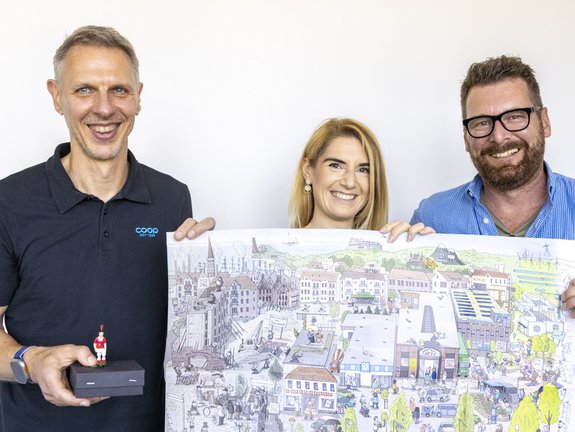 Norman, Sophie und Andreas stehen mit einem Poster vor einer weißen Wand.