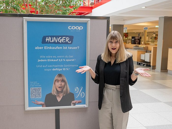 Paulina, Mitarbeiterin der coop, steht neben einem blauen Werbeplakat in der Mensa der CAU Kiel.