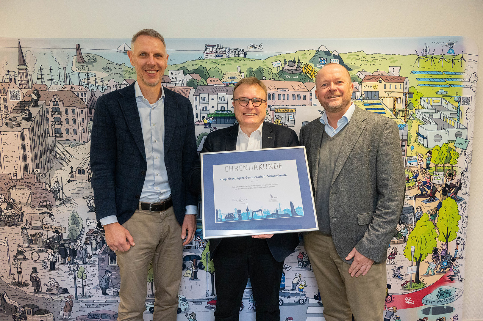 Norman Boje (Vorstandsmitglied coop eG), Marcus Schween (stellv. Hauptgeschäftsführer IHK) und Gregor Bunde (Vorstandsmitglied coop eG) Posieren mit der Ehrenurkunde vor dem coop Wimmelbildaufsteller.