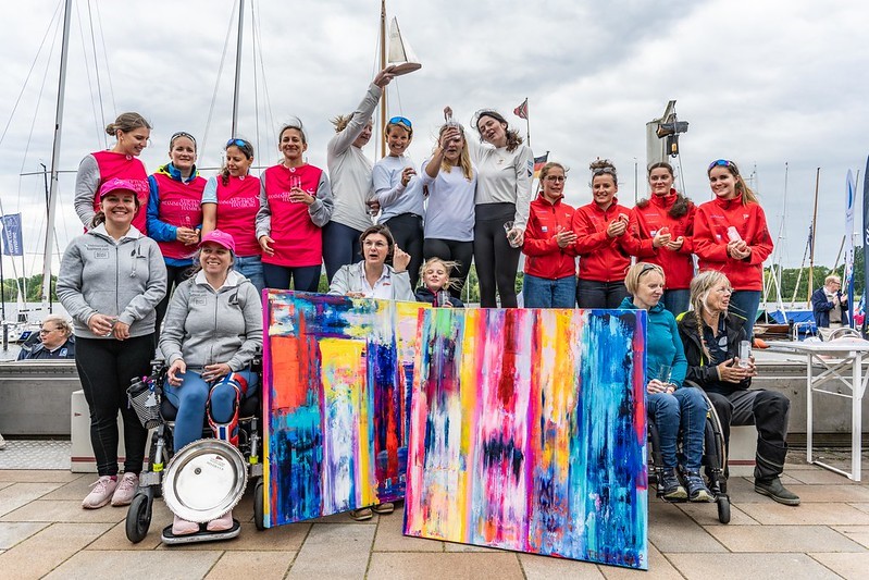 18 Frauen stehen auf dem Pier und freuen sich über ihren Sieg.